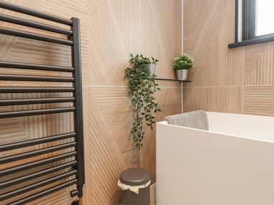 A bathroom corner with a white bathtub a gray towel a black towel warmer two potted plants on a wall shelf and a gray trash bin at Encil Gyfrinfa in Gwynus near Llithfaen