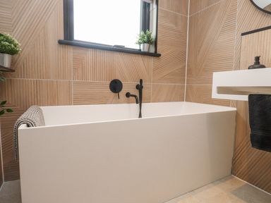 A bathroom with a white bathtub black faucet plants on windowsill and towel at Encil Gyfrinfa in Gwynus near Llithfaen