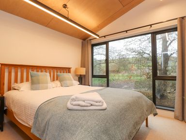 A bedroom with a wooden bed and large windows overlooking trees at Encil Gyfrinfa in Gwynus near Llithfaen