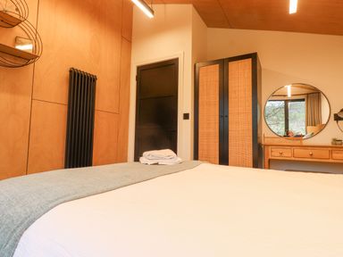 A bedroom with a bed a black door a wardrobe a round mirror and a wooden dresser at Encil Gyfrinfa in Gwynus near Llithfaen