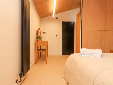 A bedroom with a bed covered in a beige blanket and a wooden vanity with a round mirror and lamp at Encil Gyfrinfa in Gwynus near Llithfaen