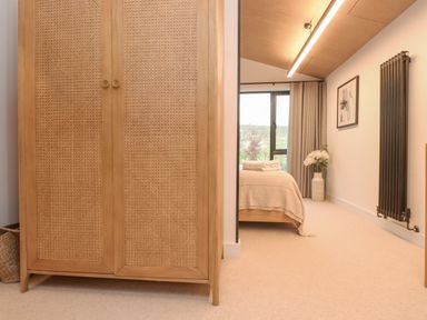 A bedroom with a wooden wardrobe bed with folded towels vase with flowers radiator and window at Encil Gyfrinfa in Gwynus near Llithfaen