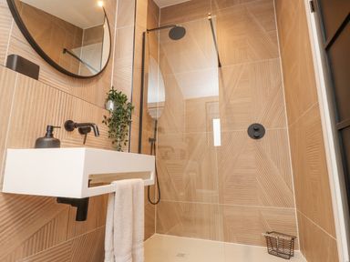 A bathroom with a white wall-mounted sink and towel hanging below a round mirror and a walk-in shower at Encil Gyfrinfa in Gwynus near Llithfaen