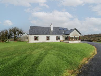 A single story house with multiple windows and solar panels on the roof surrounded by a green lawn and a paved driveway at Bunny Lane in Cloonflynn near Ballycarra County Mayo