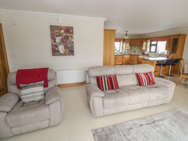 A living room with gray sofas red and gray pillows a red throw a painting of flowers on the wall and a kitchen with wooden cabinets and bar stools in the background at Bunny Lane in Cloonflynn near Ballycarra County Mayo