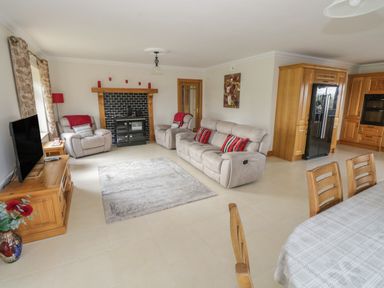 A living room with gray sofas and armchairs a black wood-burning stove wooden cabinets and a dining table at Bunny Lane in Cloonflynn near Ballycarra County Mayo