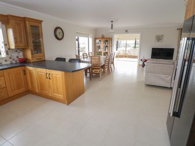 A kitchen with wooden cabinets and black countertop next to a dining area with a wooden table and chairs and a sitting area with a TV at Bunny Lane Cloonflynn near Ballycarra County Mayo