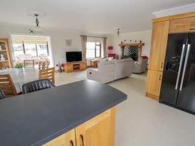 An open plan living space with a black countertop island wooden dining table chairs beige sofas a television and a black refrigerator at Bunny Lane in Cloonflynn near Ballycarra County Mayo
