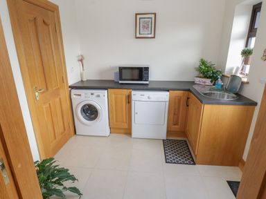 A laundry room with a washing machine dryer microwave sink and wooden cabinets at Bunny Lane Cloonflynn near Ballycarra County Mayo
