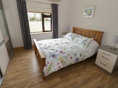 A bedroom with a wooden bed with floral bedding two nightstands with lamps a window with gray curtains and a wooden floor at Bunny Lane in Cloonflynn near Ballycarra County Mayo