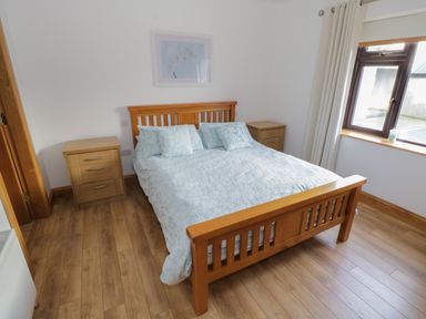 A bedroom with a wooden bed with blue bedding two wooden bedside tables a window with curtains and wooden flooring at Bunny Lane in Cloonflynn near Ballycarra County Mayo