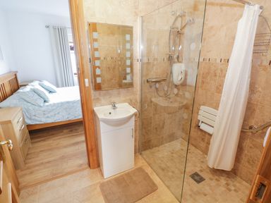 A bathroom with a shower area a sink with cabinet and a mirror next to a bedroom with a bed and a wooden dresser at Bunny Lane Cloonflynn near Ballycarra County Mayo