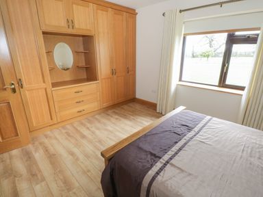 A bedroom with wooden wardrobes a bed with brown and beige bedding and a window with curtains at Bunny Lane in Cloonflynn near Ballycarra County Mayo