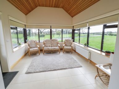 A sunroom with three armchairs a small table with a lamp a rug and large windows at Bunny Lane in Cloonflynn near Ballycarra County Mayo