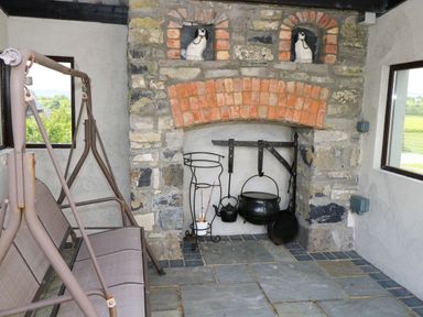 A stone fireplace with hanging pots and kettles next to a metal swing seat in a room with windows at Bunny Lane in Cloonflynn near Ballycarra County Mayo