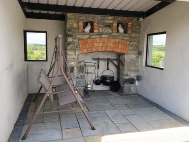 A covered outdoor area with a stone fireplace swing seat and windows showing countryside views at Bunny Lane Cloonflynn near Ballycarra County Mayo