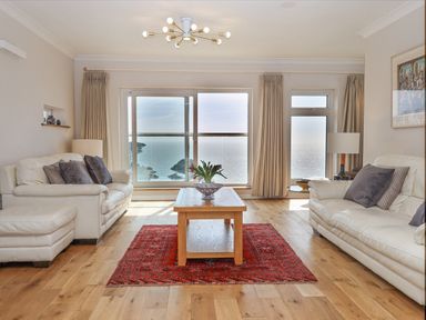 A living room with two white sofas a wooden coffee table a red rug and large windows overlooking the sea at Seahaze in Downderry