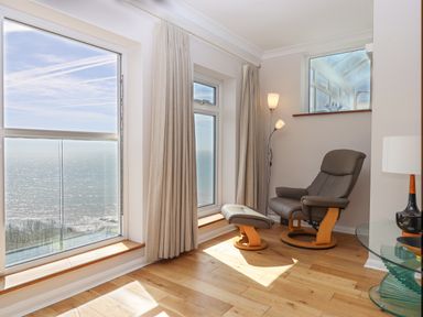 A sitting area with a recliner chair footstool floor lamp and large windows overlooking the sea at Seahaze in Downderry