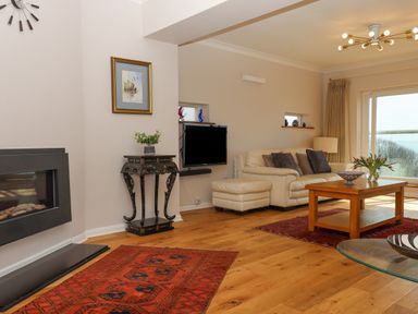 A living room with a cream sofa and ottoman a wooden coffee table and a corner fireplace at Seahaze in Downderry