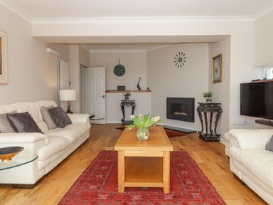 A living room with white sofas red rug wooden coffee table and a wall-mounted fireplace at Seahaze in Downderry