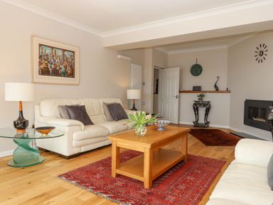 A living room with white sofas a wooden coffee table with flowers on a red rug at Seahaze in Downderry