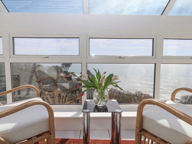 A sunroom with two chairs and a small table with flowers by the window overlooking the sea at Seahaze in Downderry