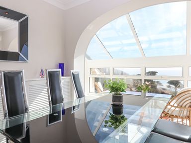 A dining area with a glass table and black chairs next to large windows with a view at Seahaze in Downderry
