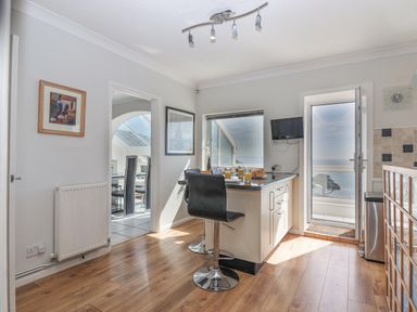 A kitchen with a breakfast bar, stools, a wall-mounted tv, and a door leading to a balcony with ocean views at Seahaze in Downderry