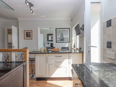 A kitchen with a black countertop island with croissants and glasses of orange juice and black chairs at Seahaze Downderry