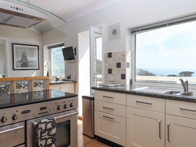 A kitchen with a stove sink cabinets and a window showing a sea view at Seahaze in Downderry