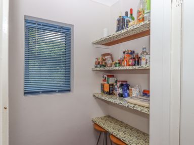 A pantry with shelves holding various food and drink items and two stools at Seahaze in Downderry