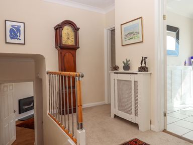 A hallway with a wooden grandfather clock a small white radiator cover with decorations and two doorways at Seahaze in Downderry