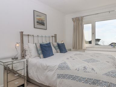 A bedroom with a double bed blue and white bedding two bedside tables with lamps a window with striped curtains and a framed picture above the bed at Seahaze in Downderry