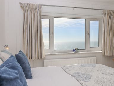 A bedroom with blue pillows a patterned quilt and a window with a sea view at Seahaze in Downderry