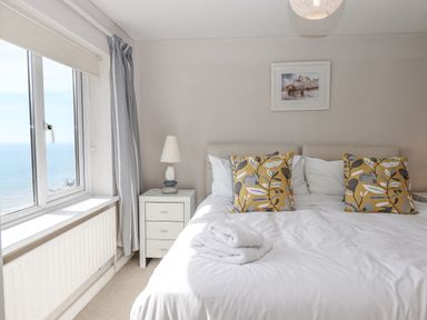 A bedroom with a bed with pillows and folded towels a bedside table with a lamp and a window with a sea view at Seahaze in Downderry