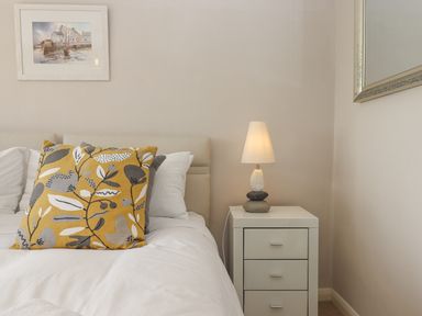 A bedroom with a bed with pillows a bedside table with a lamp and a framed picture on the wall at Seahaze in Downderry