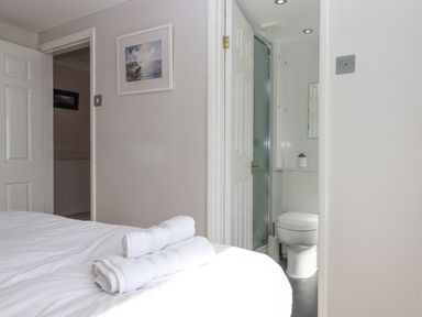 A bedroom with white towels on a bed and an open door showing a bathroom with a toilet and shower at Seahaze in Downderry