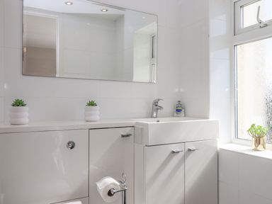 A bathroom sink with cabinets below a mirror and a window with a plant on the sill at Seahaze in Downderry