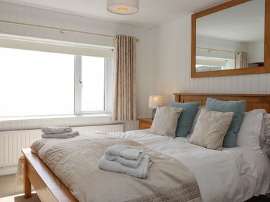 A bedroom with a bed with pillows and folded towels by a window at Seahaze in Downderry
