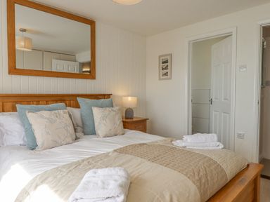 A bedroom with a wooden bed frame beige bedding pillows a nightstand with a lamp and towels on the bed at Seahaze in Downderry