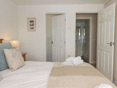 A bedroom with a bed pillows and folded towels on the bed two doors one leading to a bathroom at Seahaze in Downderry