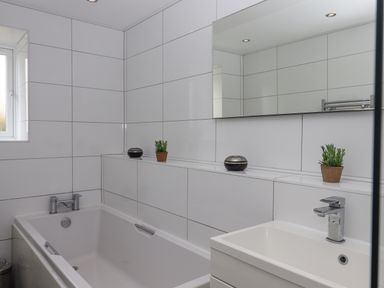 A bathroom with a bathtub a sink a mirror two small potted plants and two round containers at Seahaze in Downderry