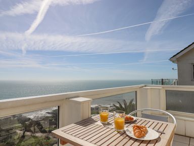 A balcony with a wooden table holding two plates with croissants and two glasses of orange juice overlooking the sea at Seahaze in Downderry