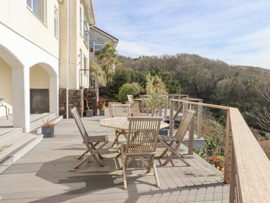 An outdoor wooden deck with a round table and chairs overlooking trees and hills at Seahaze in Downderry