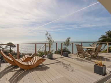 A wooden deck with lounge chairs table and four chairs with sea view at Seahaze in Downderry