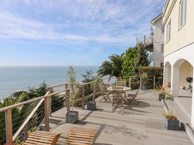 An outdoor deck with wooden chairs and tables overlooking the ocean at Seahaze in Downderry