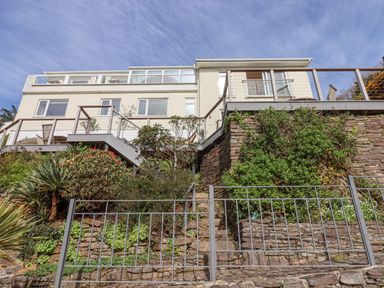 A modern house with large windows and terraces overlooking a tiered garden with plants and stone walls at Seahaze in Downderry