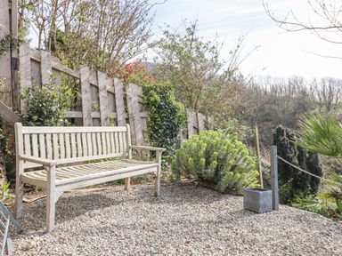 An outdoor gravel area with a wooden bench and a wooden fence surrounded by plants at Seahaze in Downderry