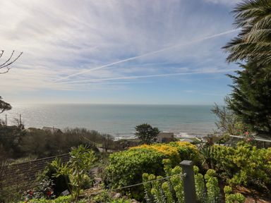 A garden with bushes and trees overlooking the ocean under a partly cloudy sky at Seahaze in Downderry