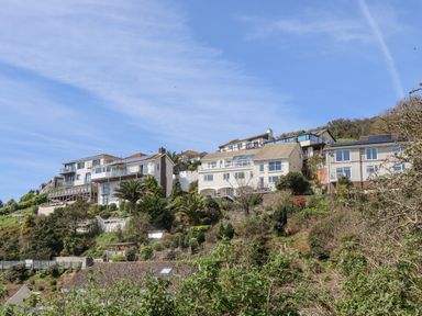 Houses on a hillside with trees and shrubs under a blue sky at Seahaze in Downderry